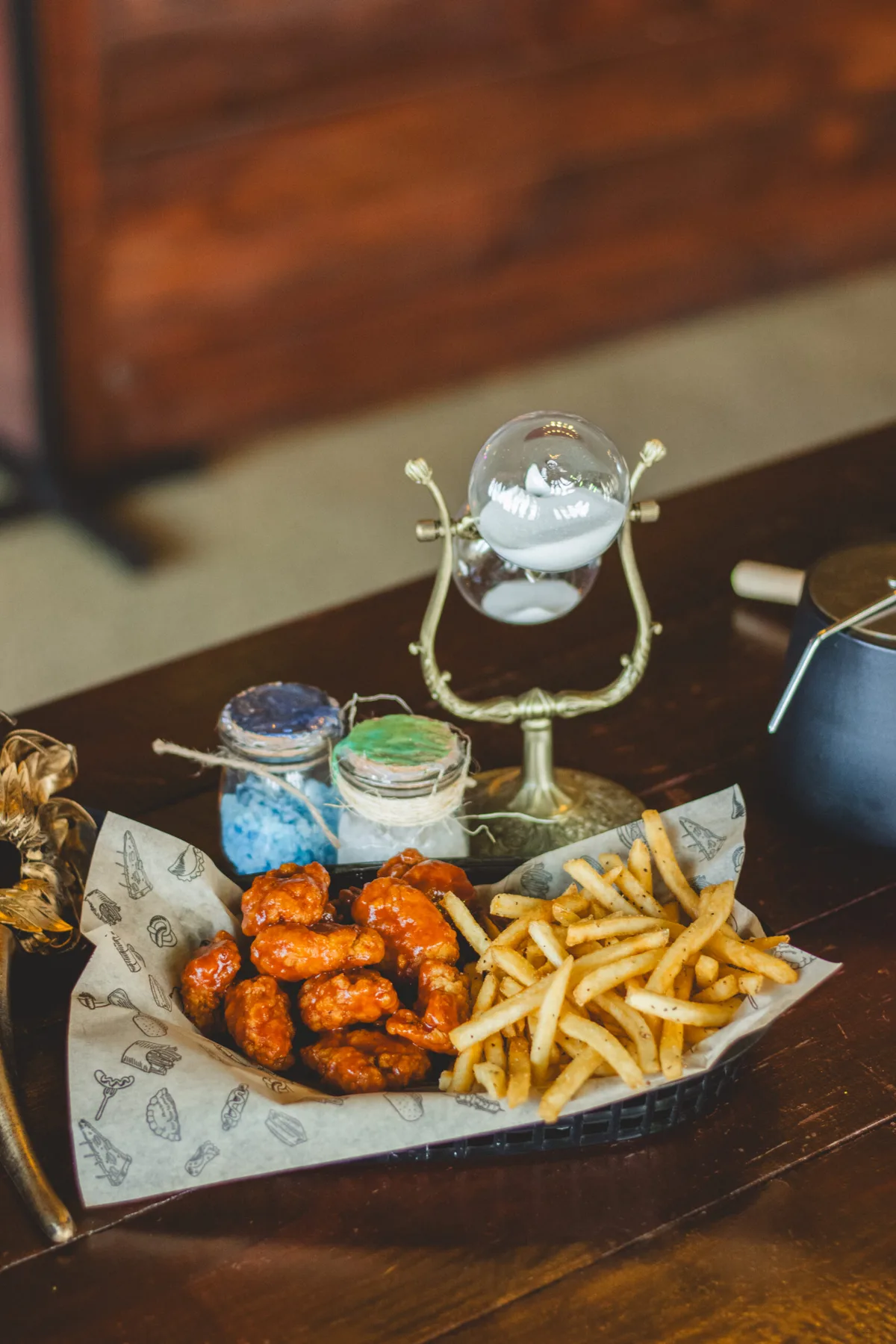 Alitas con papas junto a un reloj de arena y frascos de alquimia en Arcanum Domus
